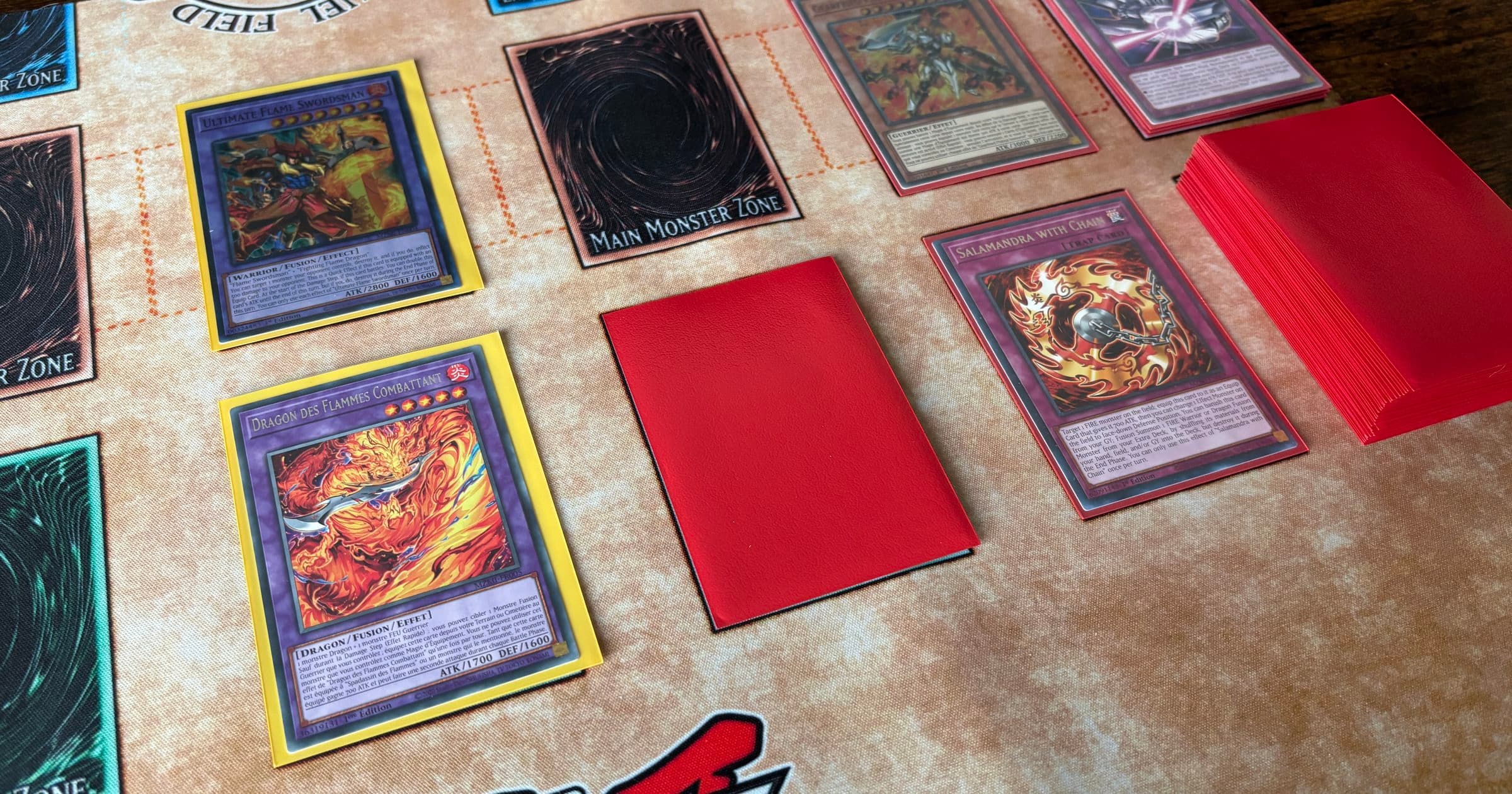 Partie de Yu-Gi-Oh! en cours sur un tapis de jeu : Dragon des Flammes Combattant, Salamandra with Chain et cartes face cachée